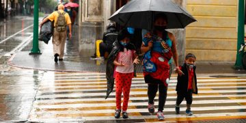 Familia guatemalteca de cubre de la lluvia con un paraguas, mientras transita por la 6 avenida de la ciudad capital./Foto: DCA.