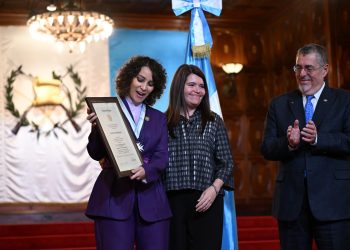 La cantautora Gaby Moreno contempla el reconocimiento que recibe de manos del presidente Bernardo Arévalo y de la secretaria privada de la Presidencia, Glenda Tager. /Foto: Byron de la Cruz