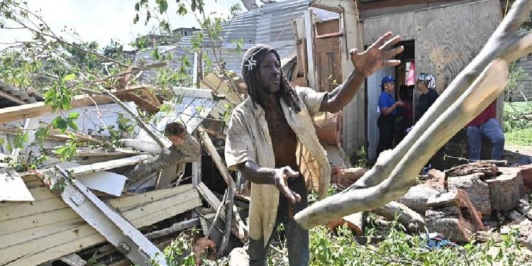Un jamaicano trata de despejar lo que quedó de su vivienda que quedó destruida al caerle un árbol por el paso del huracán Melissa.