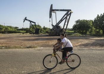 Una mujer conduce junto a un niño una bicicleta frente a balancines petroleros este jueves, en Cabimas (Venezuela). / Foto: EFE.