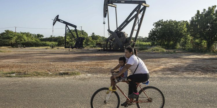 Una mujer conduce junto a un niño una bicicleta frente a balancines petroleros este jueves, en Cabimas (Venezuela). / Foto: EFE.