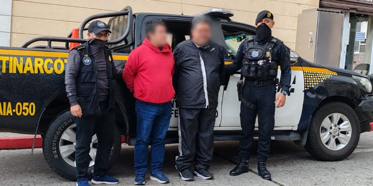 Agentes de la PNC custodian a los dos detenidos durante el allanamiento relacionado con una investigación por presunta falsificación de documentos. / Foto: PNC.