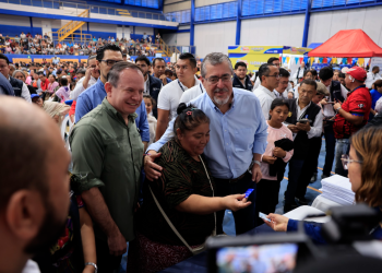 Una beneficiaria sostiene una tarjeta junto al presidente Bernardo Arévalo y al ministro Abelardo Pinto durante la actividad de Bolsa Social.
