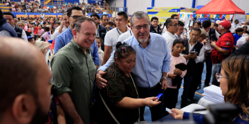 Una beneficiaria sostiene una tarjeta junto al presidente Bernardo Arévalo y al ministro Abelardo Pinto durante la actividad de Bolsa Social.
