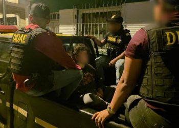 Agentes con chalecos de la DIDAE custodian a un hombre con el rostro difuminado en la parte trasera de una patrulla.