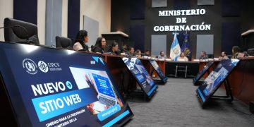 Participantes reunidos en una sala del Ministerio de Gobernación, con pantallas que anuncian el nuevo sitio web de la UPCV.