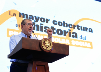 Presidente Bernardo Arévalo habla desde un podio con el escudo nacional, frente a una pantalla sobre la cobertura de Bolsa Social.