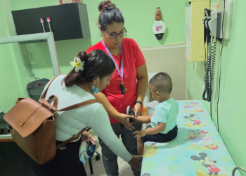 Niño sentado en una camilla recibe atención de una trabajadora de salud junto a una mujer que lo acompaña.