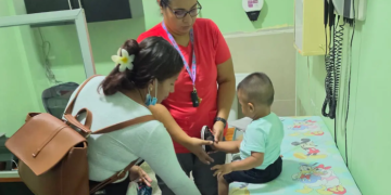 Niño sentado en una camilla recibe atención de una trabajadora de salud junto a una mujer que lo acompaña.