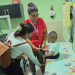 Niño sentado en una camilla recibe atención de una trabajadora de salud junto a una mujer que lo acompaña.