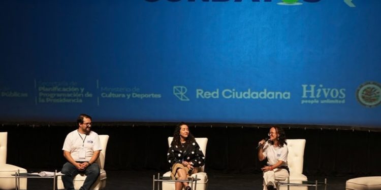 Tres panelistas conversan en un escenario frente a una pantalla con el nombre de Abrelatam/ConDatos.