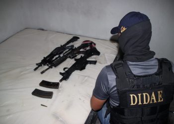 Investigador de la DIDAE frente a armas de fuego y cargadores colocados sobre una cama.