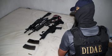 Investigador de la DIDAE frente a armas de fuego y cargadores colocados sobre una cama.
