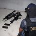 Investigador de la DIDAE frente a armas de fuego y cargadores colocados sobre una cama.