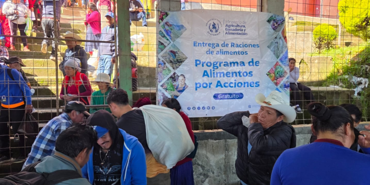 Personas trasladan sacos junto a una manta del MAGA que anuncia la entrega gratuita de alimentos del programa Alimentos por Acciones.