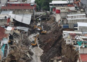 Excavadoras en el cauce de un río, entre viviendas con daños y taludes de tierra expuestos.