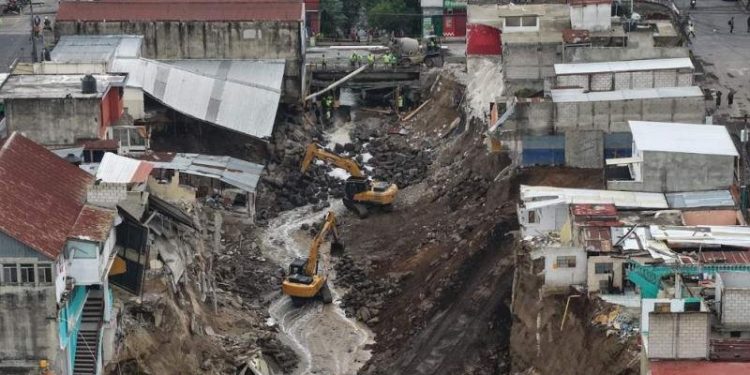 Excavadoras en el cauce de un río, entre viviendas con daños y taludes de tierra expuestos.