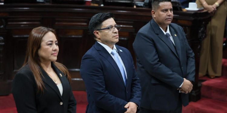 Tres personas con vestimenta formal permanecen de pie en el hemiciclo del Congreso de la República.