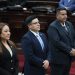 Tres personas con vestimenta formal permanecen de pie en el hemiciclo del Congreso de la República.