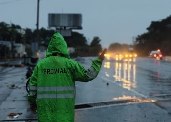 Brigadista de Provial dirige el tránsito vehicular bajo la lluvia en una carretera mojada.