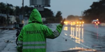 Brigadista de Provial dirige el tránsito vehicular bajo la lluvia en una carretera mojada.