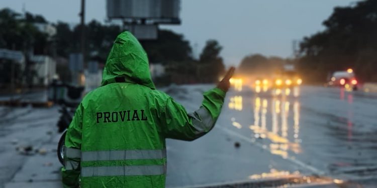 Brigadista de Provial dirige el tránsito vehicular bajo la lluvia en una carretera mojada.