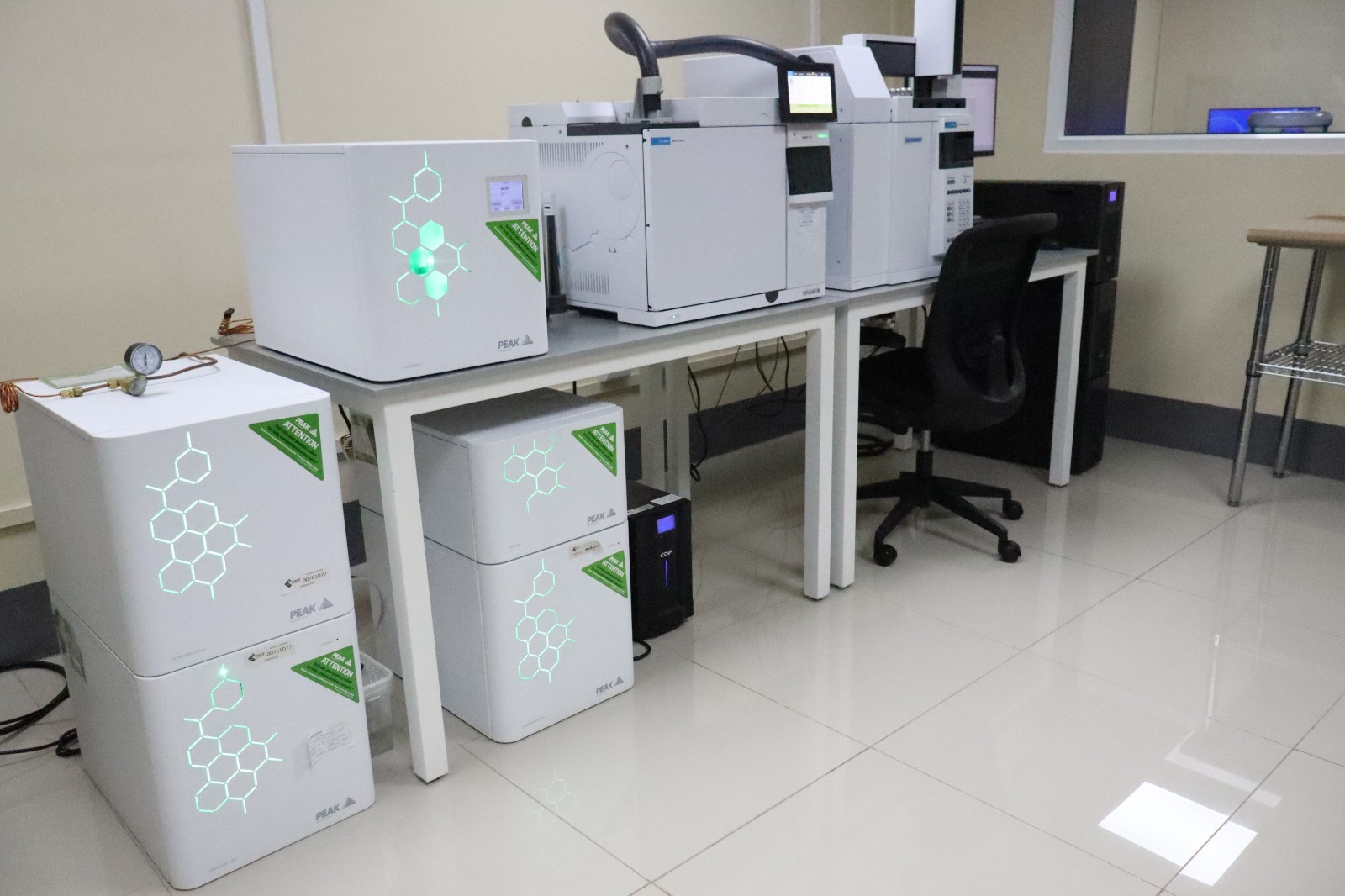 Equipos de laboratorio distribuidos sobre y debajo de mesas de trabajo, junto a monitores y una silla.