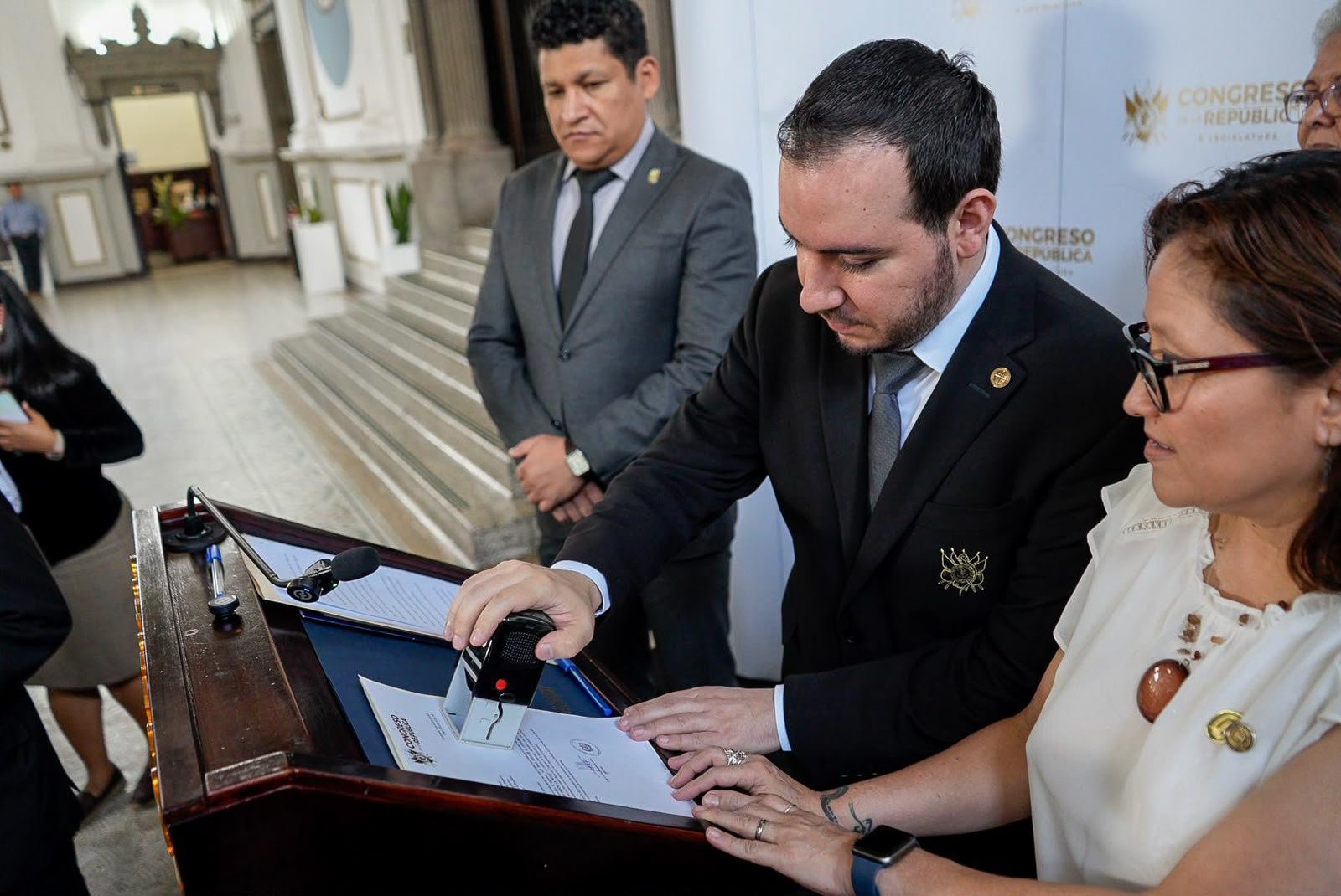 Un hombre coloca un sello en un documento sobre un atril del Congreso, acompañado de otras personas.