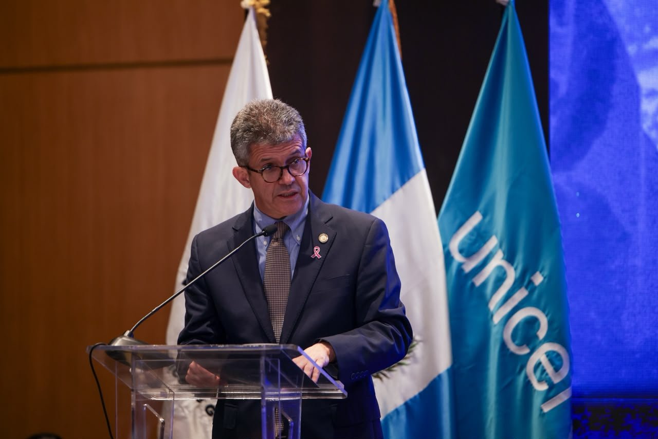 Joaquín Barnoya interviene ante un micrófono, con las banderas de Guatemala y Unicef detrás.
