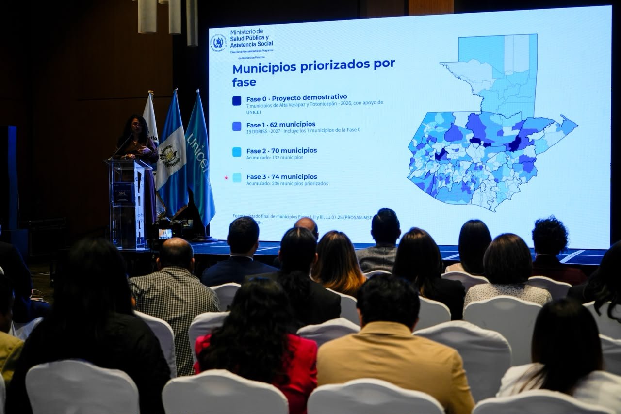 Una expositora presenta un mapa de Guatemala con municipios diferenciados por fases, ante un público sentado.