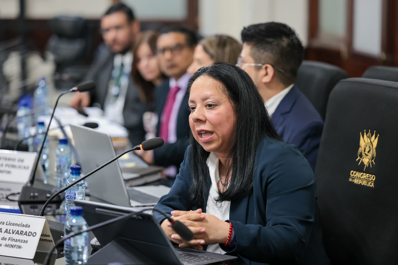 Débora Alvarado habla frente a un micrófono durante una reunión en el Congreso, acompañada por la delegación del Minfin.