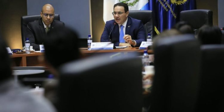 Marco Antonio Villeda habla ante un micrófono durante una reunión, frente a los asistentes y junto a otro participante.