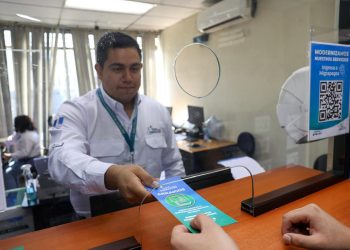 Trabajador del IGM entrega un folleto sobre arraigos a una persona en una ventanilla de atención.