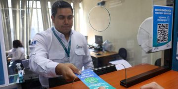 Trabajador del IGM entrega un folleto sobre arraigos a una persona en una ventanilla de atención.