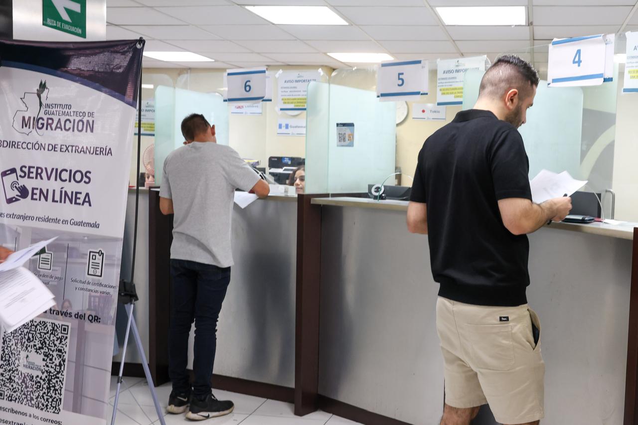 Dos hombres con documentos frente a las ventanillas de atención de la Subdirección de Extranjería del IGM.