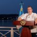 Bernardo Arévalo habla desde un atril con el escudo nacional, junto a la bandera de Guatemala y con un lago al fondo.