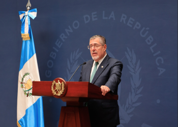 Presidente Bernardo Arévalo ante un atril con el escudo nacional, junto a la bandera de Guatemala.