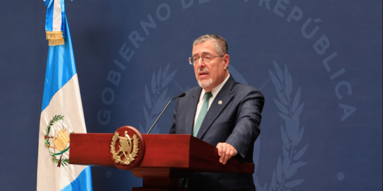 Presidente Bernardo Arévalo ante un atril con el escudo nacional, junto a la bandera de Guatemala.