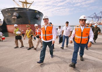 Bernardo Arévalo camina por el muelle de Puerto Quetzal junto a una comitiva civil y militar, con un buque al fondo.