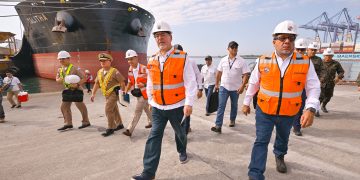 Bernardo Arévalo camina por el muelle de Puerto Quetzal junto a una comitiva civil y militar, con un buque al fondo.