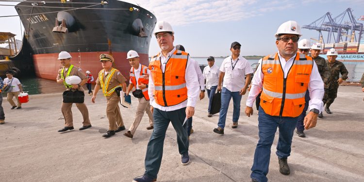 Bernardo Arévalo camina por el muelle de Puerto Quetzal junto a una comitiva civil y militar, con un buque al fondo.