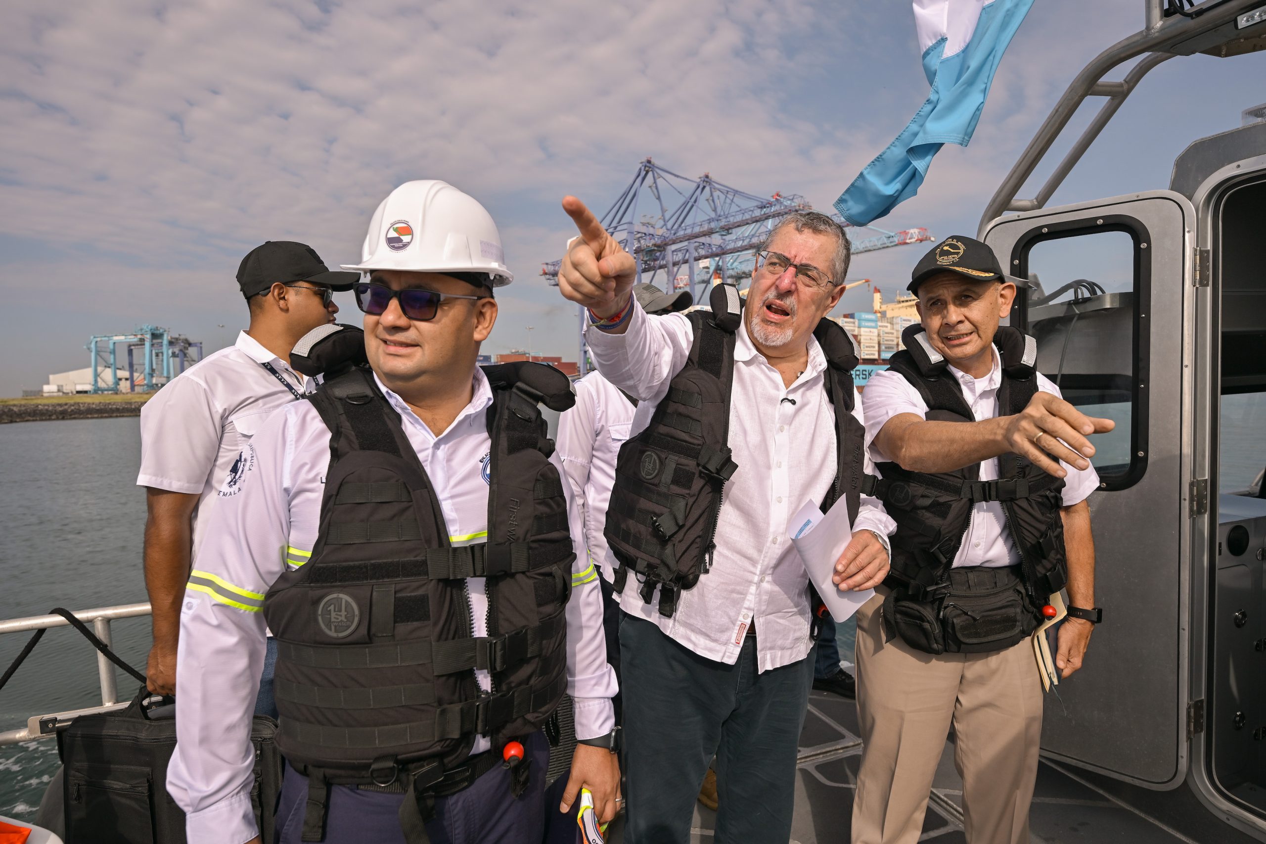 Bernardo Arévalo señala hacia las instalaciones de Puerto Quetzal desde una embarcación, acompañado por integrantes de la comitiva.