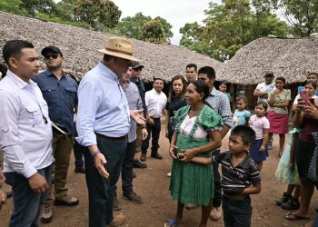 El presidente Bernardo Arévalo conversa con una mujer junto a un niño, frente a viviendas con techos de palma.