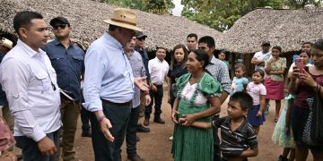 El presidente Bernardo Arévalo conversa con una mujer junto a un niño, frente a viviendas con techos de palma.