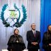 Bernardo Arévalo permanece de pie entre dos magistradas con toga, frente al escudo nacional y cortinas azules y blancas.