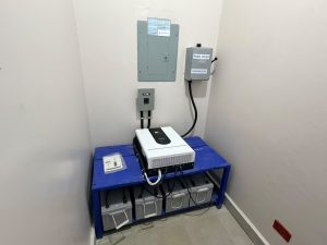 Baterías y equipos eléctricos conectados sobre una estructura metálica azul y en la pared de una habitación.