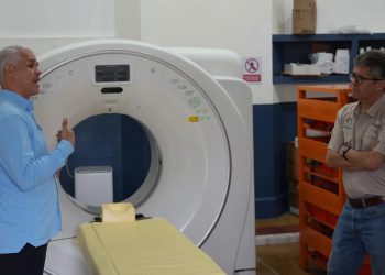 Joaquín Barnoya escucha a un acompañante junto a un tomógrafo y su camilla en el Hospital de Mazatenango.