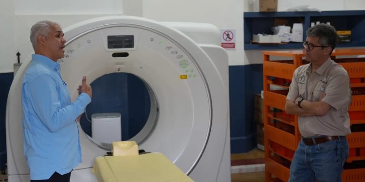 Joaquín Barnoya escucha a un acompañante junto a un tomógrafo y su camilla en el Hospital de Mazatenango.