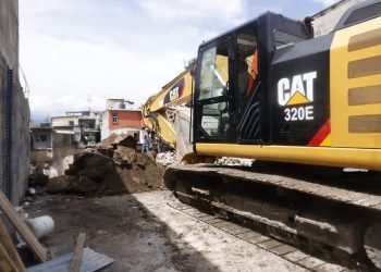 Excavadora sobre orugas junto a montículos de tierra y escombros, entre viviendas de Villa Hermosa I.