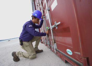 Trabajador con casco y uniforme revisa el mecanismo de cierre de un contenedor de carga.